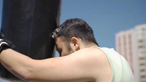 Man Rests Head Against Heavy Bag after Boxing Workout