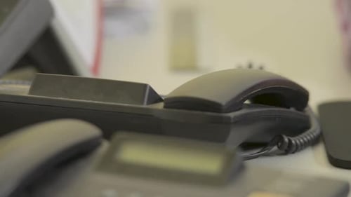 Hand picking up a black office phone, dialing swiftly, blurred background