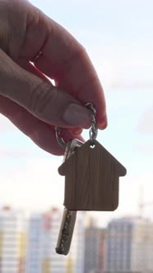 Key with House Keychain in Hand on Background with New Houses Construction House Purchase and Real