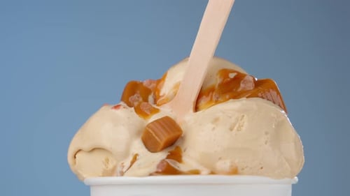 Helado de crema en taza blanca rociado con caramelo y espolvoreado con trozos de caramelo con madera