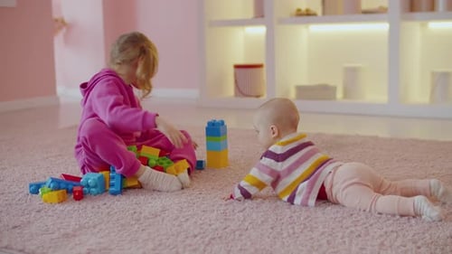 Joyful Little Girl and Infant Baby Playing with Toy Blocks at Home