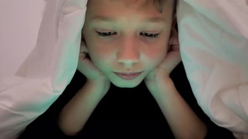 Junge spielt auf dem Tablet, während er unter der Decke liegt