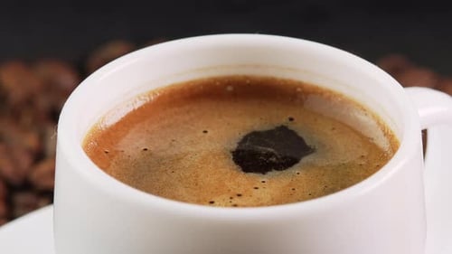 Une goutte tombant dans une tasse à café pivote parmi les grains de café torréfiés (arrière-plan, vue latérale rapprochée)