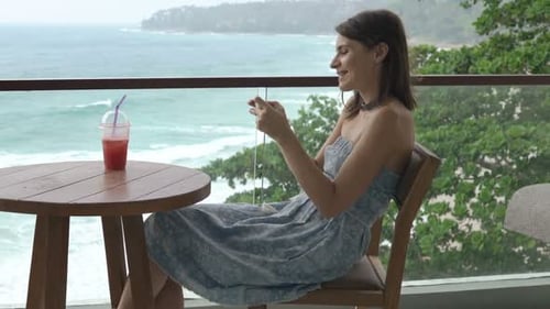 Young woman enjoys mobile game on terrace with ocean view on summer day