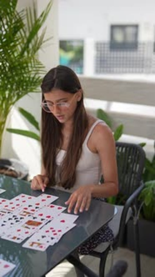 Une femme jouant au solitaire en plein air sur une table en verre se concentrant sur son jeu avec une pensée stratégique