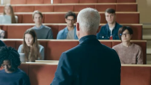 Clase frente a la cámara: un profesor destacado escribe en la pizarra y da una conferencia en un aula