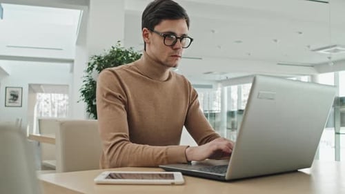 Young Adult Man Types on Laptop in Bright Interior