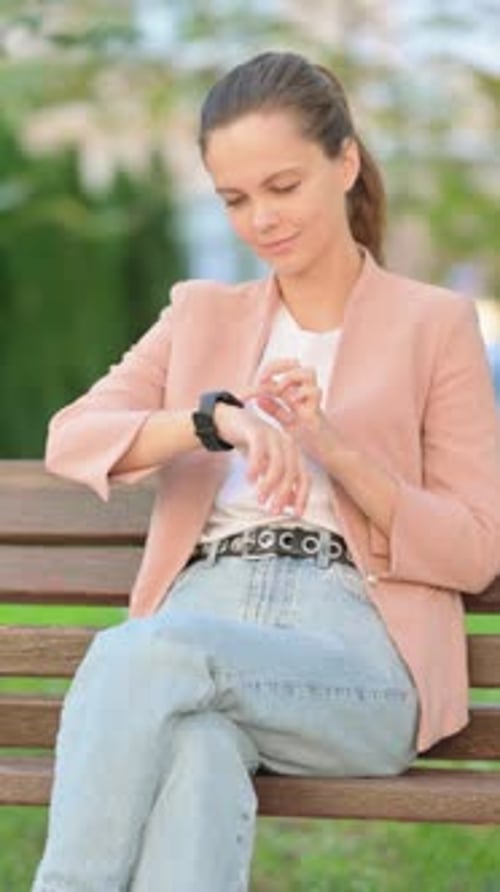 Woman Checks Smartwatch Sitting on Park Bench