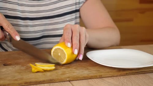 14 1Woman slicing lemon into thin round pieces on wooden board, preparing it for tea or culinary use