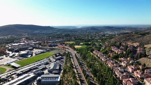 Aerial drone shot taken over a road with a huge complex on one side and residential houses on the ot