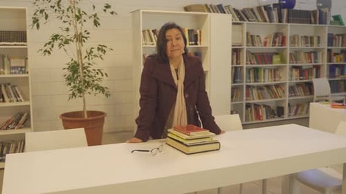 Woman Standing Behind Table of Books in Library