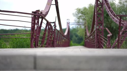 Side View Unrecognizable Man Passing on Electric Scooter at Background of Walking Bridge in Park
