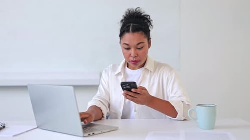 Woman Using Laptop and Cell Phone at Desk