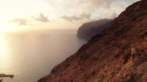 Woman in sportswear stands with arms outstretched on a rocky cliff, overlooking a serene ocean at su