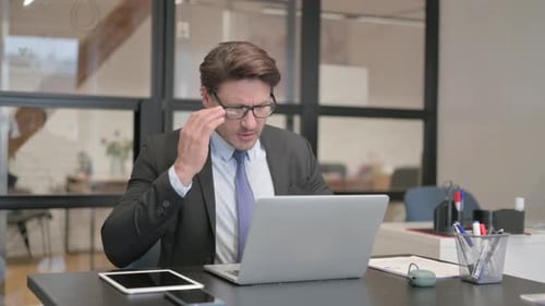 Middle Aged Businessman having Headache while Working on Laptop in Office