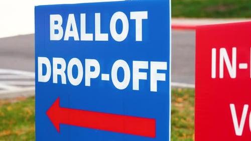 Blue Ellection Ballot Drop-off Sign with Red Arrow Pointing Left and Blowing in the Wind Outside in