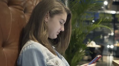 Teenage Girl Texting on Smartphone Sitting by Table in Cafe Adolescent