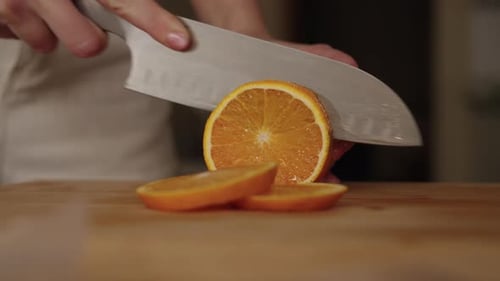 Seitenansicht einer unkenntlichen Frau, die frische Orange auf einem Holzschneidebrett in Scheiben schneidet und Zutaten zubereitet