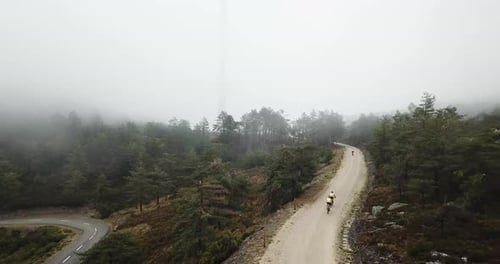 Group of cyclists going up a dirt road with intense fog. Cyclists going into a foggy forest on a mou