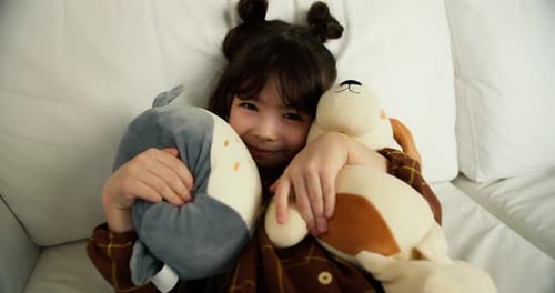 Cute Child Hugging Toys on White Couch Smiling