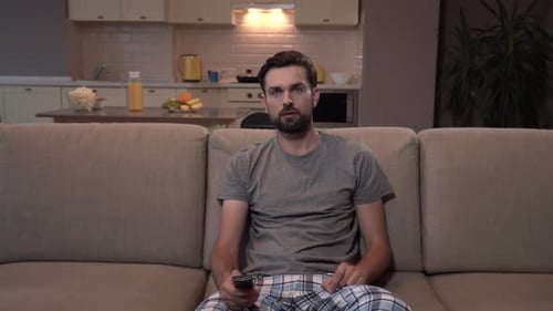 Young Man Sits on Couch With Remote