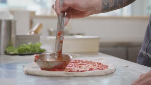 Hands of Chef Spreading Tomato Sauce with Ladle over Pizza Base