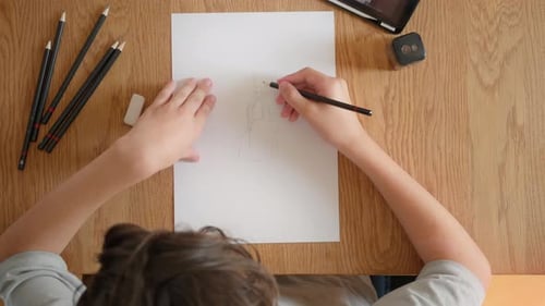 Child focused on drawing a fantasy character sketch, creative desk top view