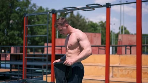 young athlete bodybuilder standing on the sports field after outdoor training takes off his shirt