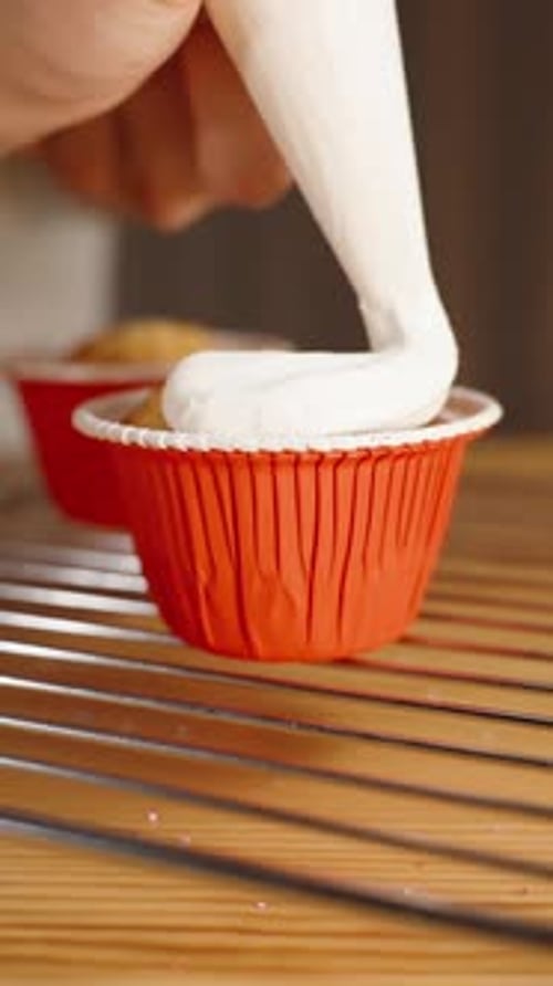 The pastry chef decorates a cupcake with white cream, squeezing it out of a piping bag. Slow motion.