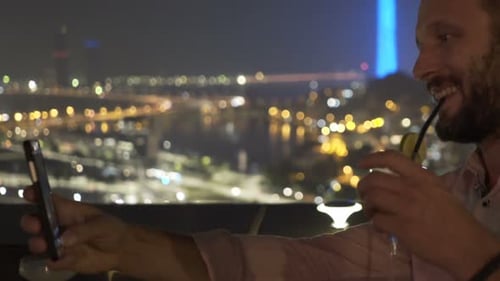 Young Man with Drink Taking Selfie with Cellphone on Terrace in Bar