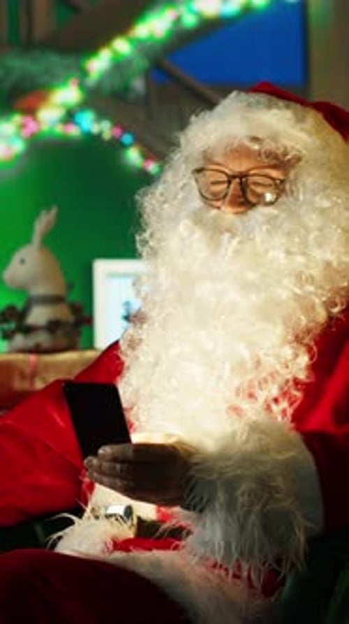 Vertical Video Happy Man Dressed As Santa Claus Looks at Letter Received From Kids on Phone