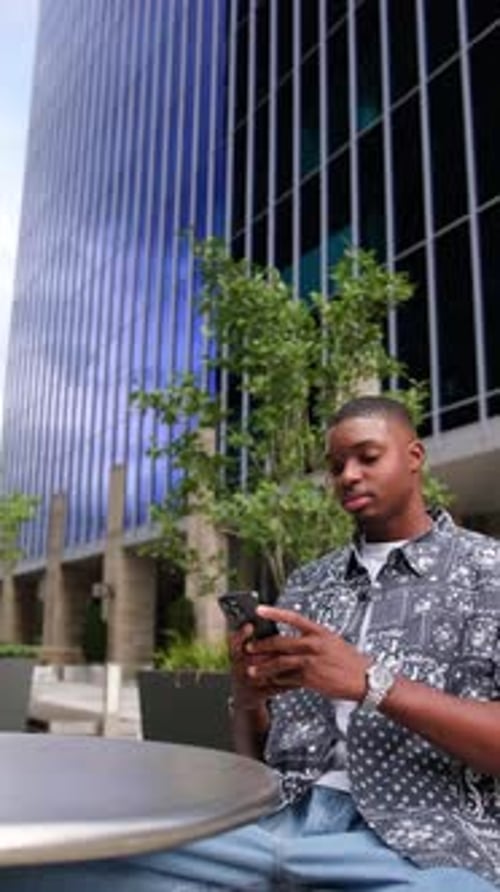 African American Man Sitting Outside in the City Using Smartphone Vertical Video