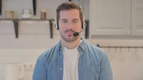 Young Man with Headset Looking toward Camera in Call Center