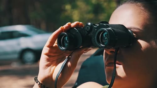 Woman looks through binoculars in forest