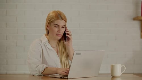 Woman Talks on Phone While Working on Laptop