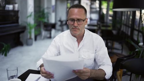 Focused Adult Businessman Working on Project Writing Paper Notes Sitting at Caffee Desk