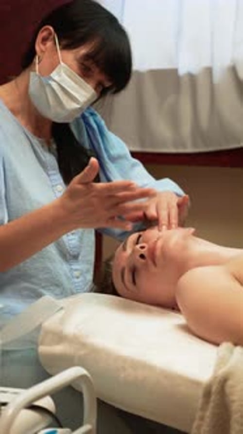 Skincare Expert in Medical Mask Providing Spiritual Facial Massage on Forehead Vertical Orientation