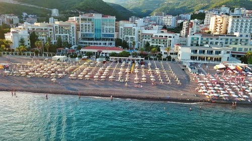 Beach with Sun Umbrellas Sunbeds and People Relaxing in the Town of Becici Near Adriatic Sea Against