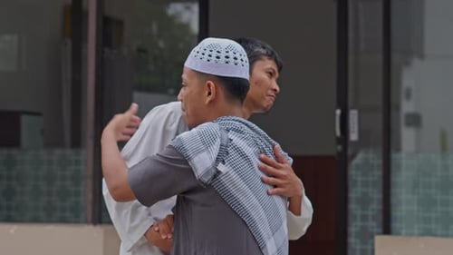 Zwei muslimische Männer begrüßen sich mit warmem Handschlag und Umarmung vor der Moschee