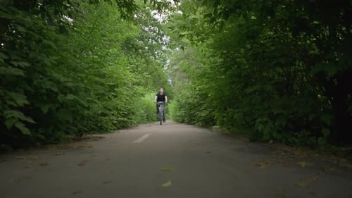 Young Boy Riding Bicycle Through Scenic Green Path Dodging Branches