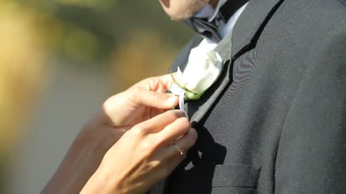 Woman Attaches Boutonniere to Groom's Suit Jacket