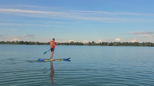 Ein Mann schwimmt stehend auf einem SUP-Board und rudert Ein junger Mann schwimmt auf einem SUP-Board auf einem See Stand Up