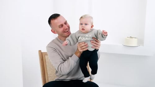 Loving Father Holding Blond Baby in Bright Room