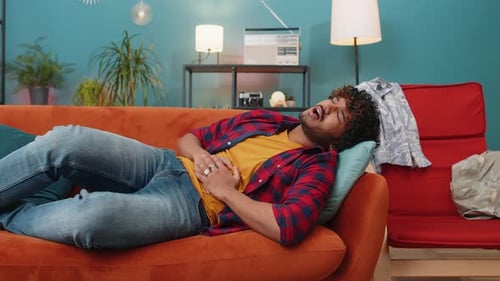 Indischer Mann liegt auf dem Sofa und verspürt plötzlich starke Bauchschmerzen, Gastritis-Problem, Durchfall