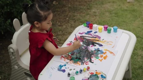 happy toddler girl painting watercolor in a paper at backyard