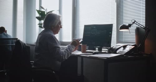 Senior-Geschäftsmann nutzt Telefon, überwacht Börse und Aktien am Computer