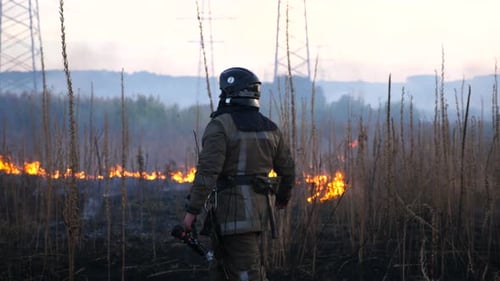 Firefighter Walking Towards Burning Field During Sunset