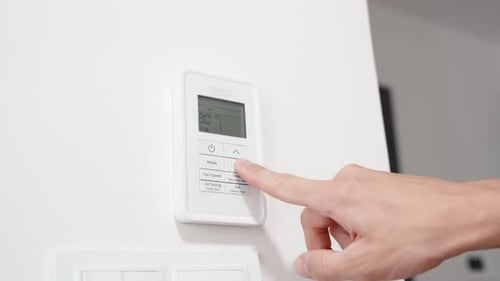 El hombre ajusta la temperatura más baja en el mando a distancia del aire acondicionado.