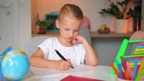 Child Kid Girl doing her homework art a desk. School girl writes in a notebook.