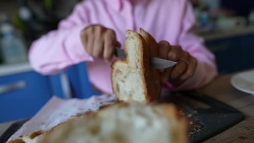 Person Slices Crusty Bread with Knife in Kitchen